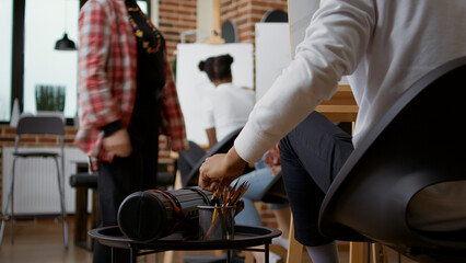 Student using colorful pencils on table to draw sketch in art class. Person taking drawing tools to create workshop masterpiece on white canvas and easel at artistic lesson. Close up