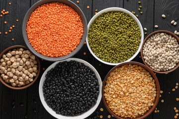 Overhead view of bowls of assorted raw legumes on a dark wooden table