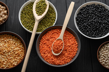 Overhead view of bowls of assorted raw legumes on a dark wooden table