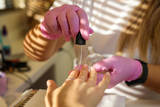 A manicurist applies oil on woman's nails and cuticles in beauty salon