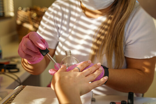 A manicurist applies oil on woman's nails and cuticles in beauty salon