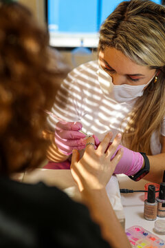 The manicurist covers her nails with a brush of clear gel nail polish