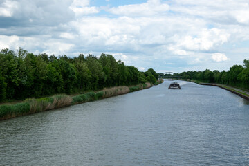 Flowing barges on the river. A bridge is visible in the distance. Green forests on the sides.