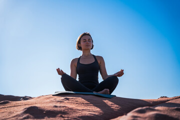 Fototapeta na wymiar Mindful girl sitting cross-legged at the sand, practicing yoga and enjoying meditation
