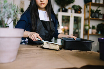 Floral worker tidying up soil from desk after replanting plants 