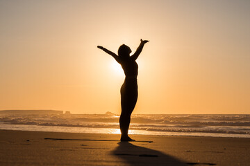 Woman doing yoga pose and greeting to sun on the seashore at sunset