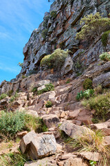 Rocky trail on a mountain with plants and grass against clear blue sky. Mysterious path or steps leading up to a summit or peak. Low angle of rough and dangerous terrain in remote location in nature