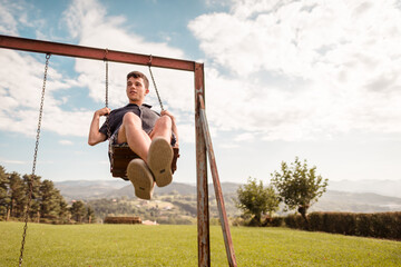 Teenage boy swinging in the park during summer
