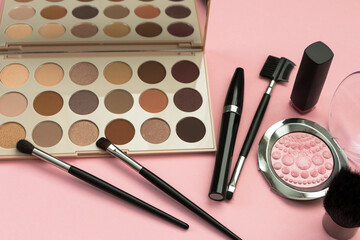 set of decorative cosmetics, eyeshadow palette, brushes, mascara on a pink background