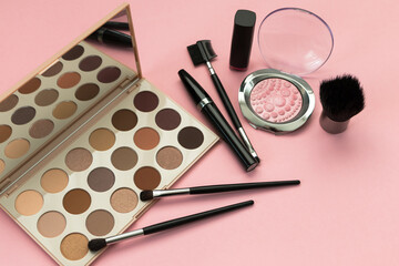 set of decorative cosmetics, eyeshadow palette, brushes, mascara on a pink background