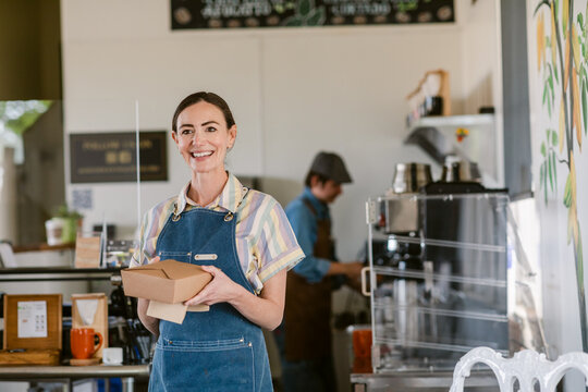 Smiling woman on apron with take out brown food box