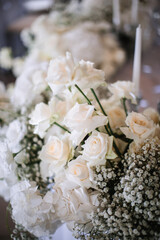 Wedding decor of a banquet table of snow-white color. White roses, peonies, gypsophila, white candles in glass candlesticks.