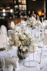 Wedding decor of a banquet table of snow-white color. White roses, peonies, gypsophila, white candles in glass candlesticks.