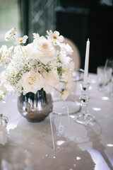 Wedding decor of a banquet table of snow-white color. White roses, peonies, gypsophila, white candles in glass candlesticks.