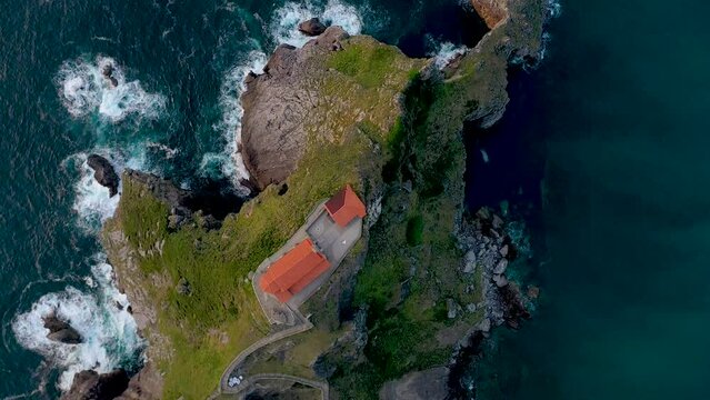 Drone rotating above the Gaztelugatxe Isle. View of San Juan de Gaztelugatxe, an hermitage dedicated to John the Baptist. Waves splashing on the rocks. Warms colours reflecting on building and water