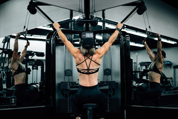 Muscular woman using machine at gym wearing black workout clothi