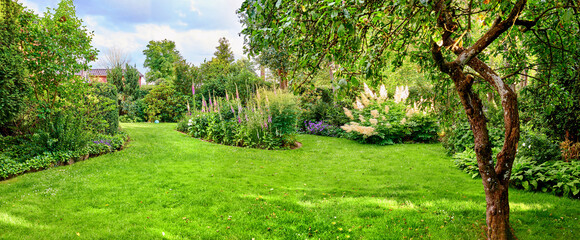 A magical and lush green garden with various colorful flowers blooming and trees growing in spring...