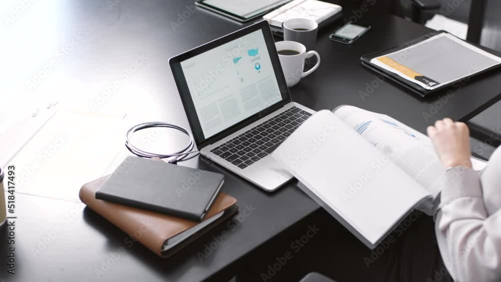 Poster a female corporate professional reading paperwork and looking at information while working at her de