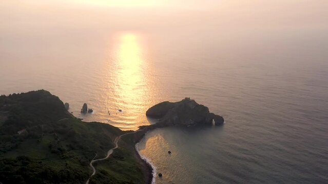 The Gaztelugatxe Isle at sunset. Underexposed video and sun reflecting on Vizcaya Golf water. Perspective from drone. Famous travel destination in North of Spain, Basque Country. Drone going forward