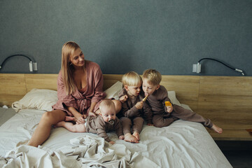Mother with three little sons eat ice cream sitting on the bed