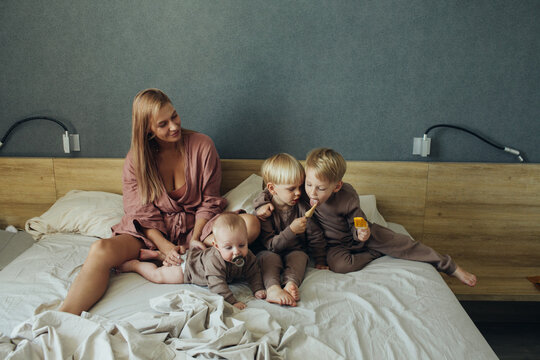 Mother with three little sons eat ice cream sitting on the bed