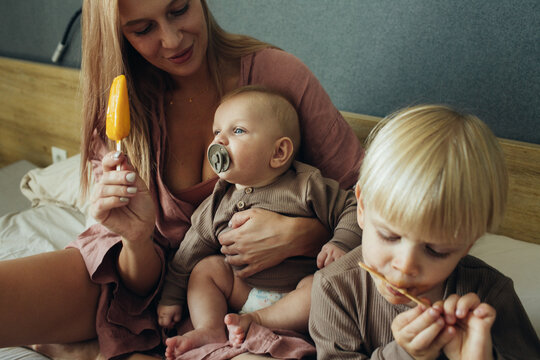 Mother with little sons eat ice cream sitting on the bed