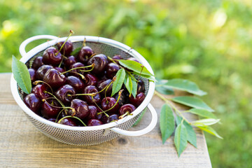 cherry berries on a wooden table in a colander, summer food, top view, place for text