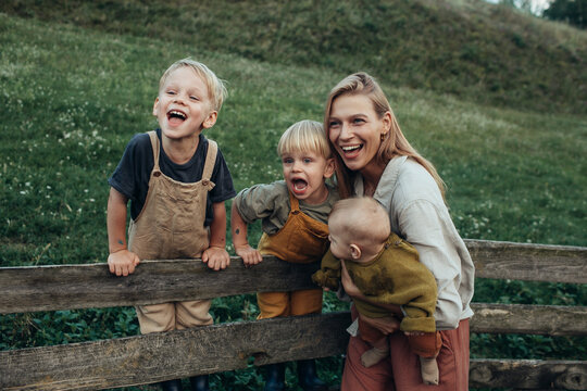 Mother with little sons are sitting on a rural fence and laughing