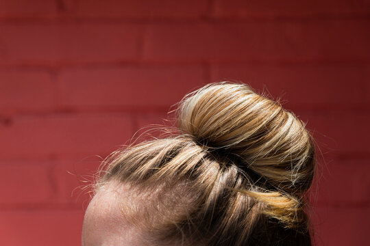 Closeup of a natural hairstyle bun of a blonde woman in a red wall