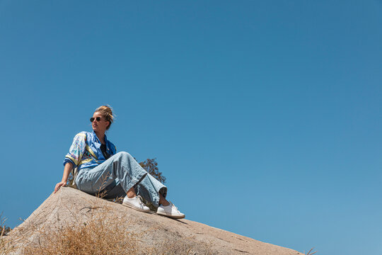 woman with her hair in a bun sitting on a giant rock with a blue sky