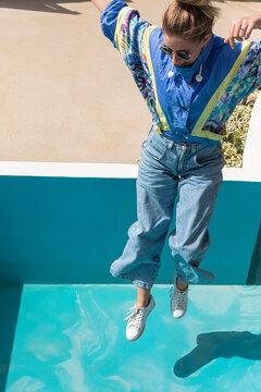 A girl wearing a 90s jacket jumping into an empty blue pool