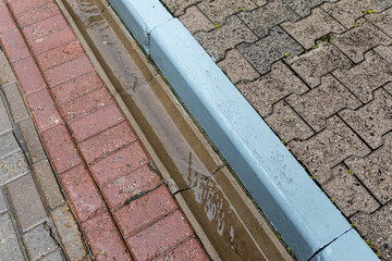 Rainwater runoff during rain. Concrete gutter for rainwater drainage between the sidewalk and the...