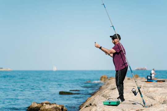 Man standing near fishing rod at seaside on sunny day