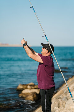 Mature male fisher unhooking caught fish on seashore