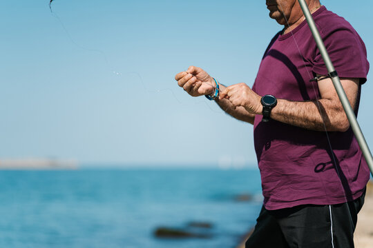 Crop man preparing fishing line near sea