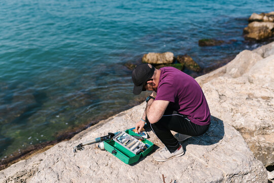 Male angler choosing tools from tackle box at seaside