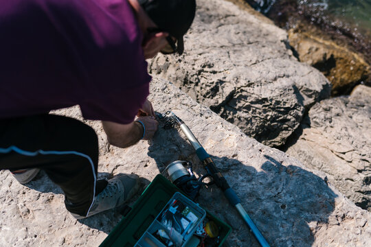 Crop fisherman attaching sinker to rod on seashore