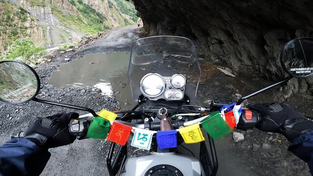 POV Motorcyclist riding motorbike by dangerous mountain off road in Himalayas. Biker on motorcycle going between mountain valley near landslides and rocks. Steering wheel view