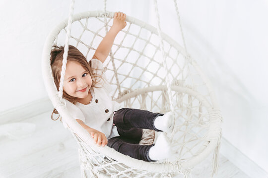 Little girl playing in a macrame swing indoors