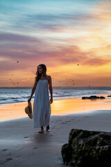 Barefooted lady walking on sandy seashore at sunset