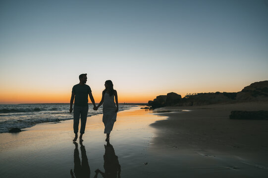 Loving couple holding hands on beach at sunset
