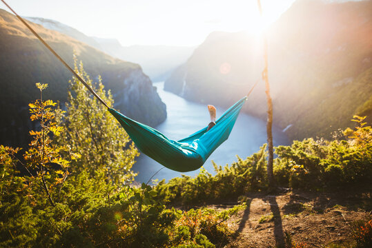 Man relaxing in hammock above Geirangerfjord at sunset - Powered by Adobe