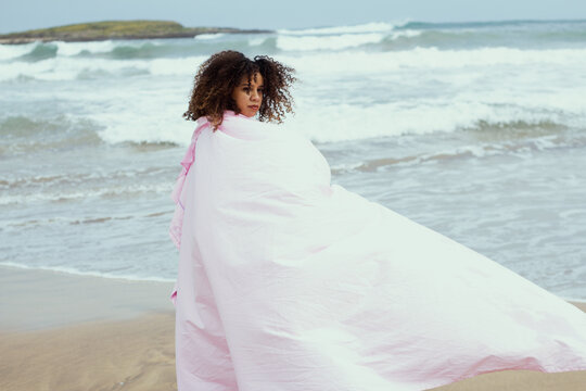 Young girl with curly hair at the beach wearing pink fabric