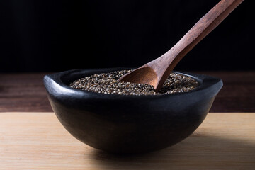 chia seeds in black ceramic bowl on black background with wooden spoon