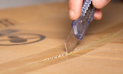 Person opening a courier delivery package with an utility knife	