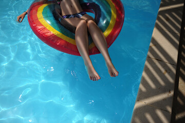 A teenage girl plays in a swimming pool with a rainbow pool float