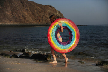 A girl plays with a raunbow coloured pool float at the beach