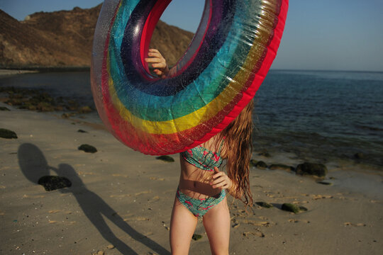 A girl plays with a raunbow coloured pool float at the beach