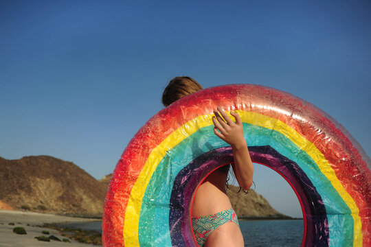 A girl plays with a raunbow coloured pool float at the beach
