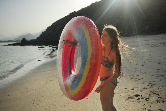 A girl plays with a raunbow coloured pool float at the beach